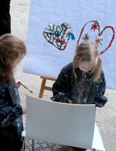 zwei etwa fünfjährige Künstlerinnen malen ein Bild auf einer großen Leinwand