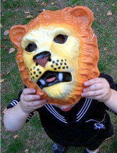 ein kleines Kind mit Löwenmaske vor dem Gesicht