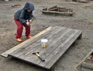 Ein kleiner Junge hält einen Hammer in der Hand und bearbeitet einige Holzbretter