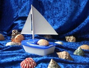 Arrangement mit Spielzeug-Segelboot und Muscheln auf einem blauen Samtstoff
