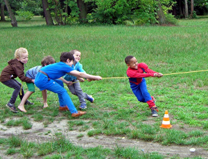 Tauziehen: 5 Kinder auf einer großen Wiese ziehen mit aller Kraft am linken Ende des Taus